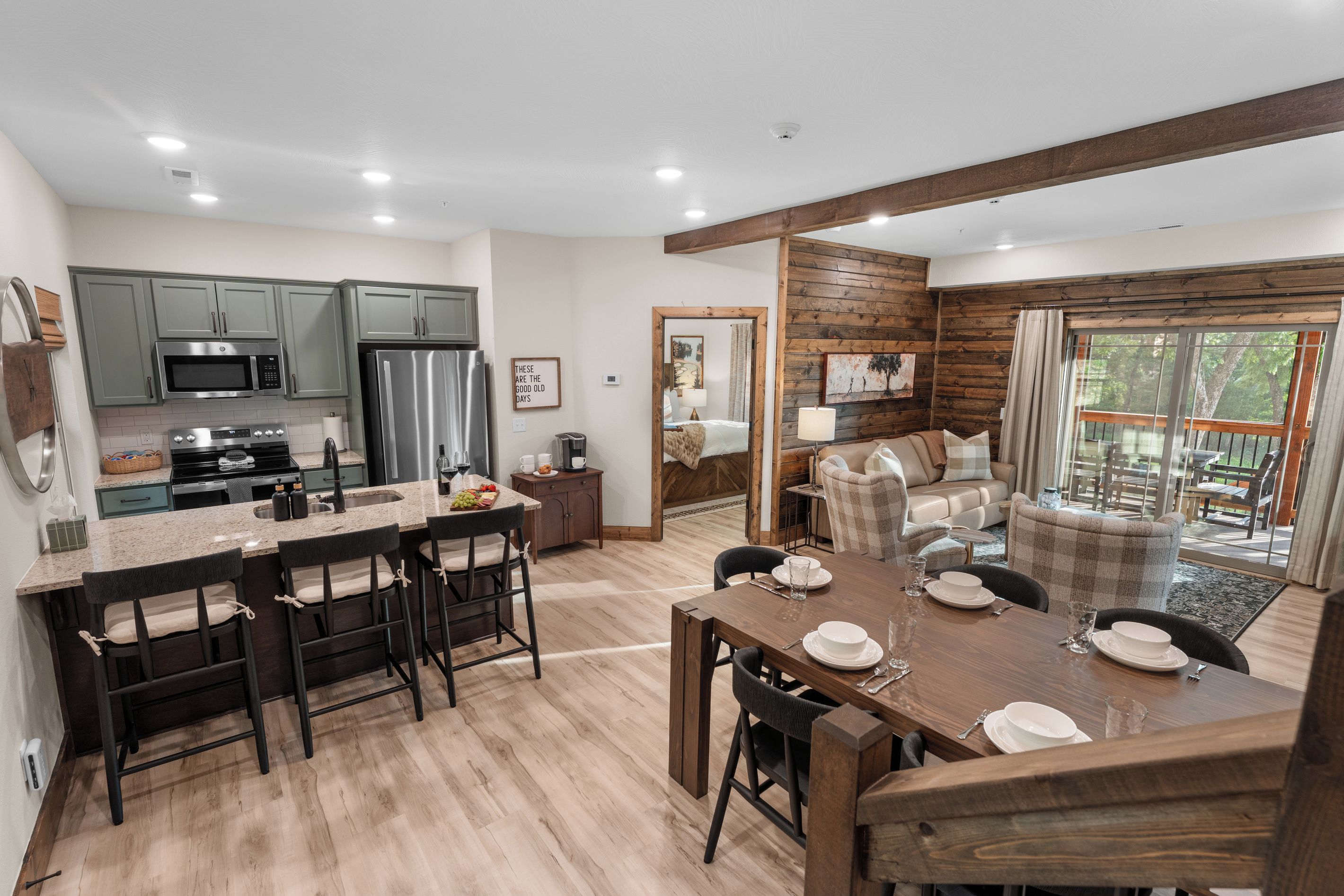 A modern kitchen with a central island, dining area with a wooden table, and a cozy seating area with a view of the outdoors.