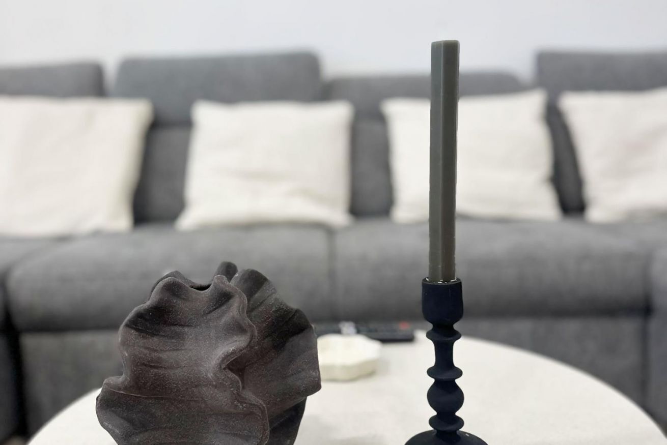 Een moderne woonkamer met een grijze bank, witte kussens, een witte salontafel, en een decoratief zwart object.