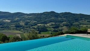 Piscina infinita azul límpida com vista para colinas ondulantes e um morro distante.