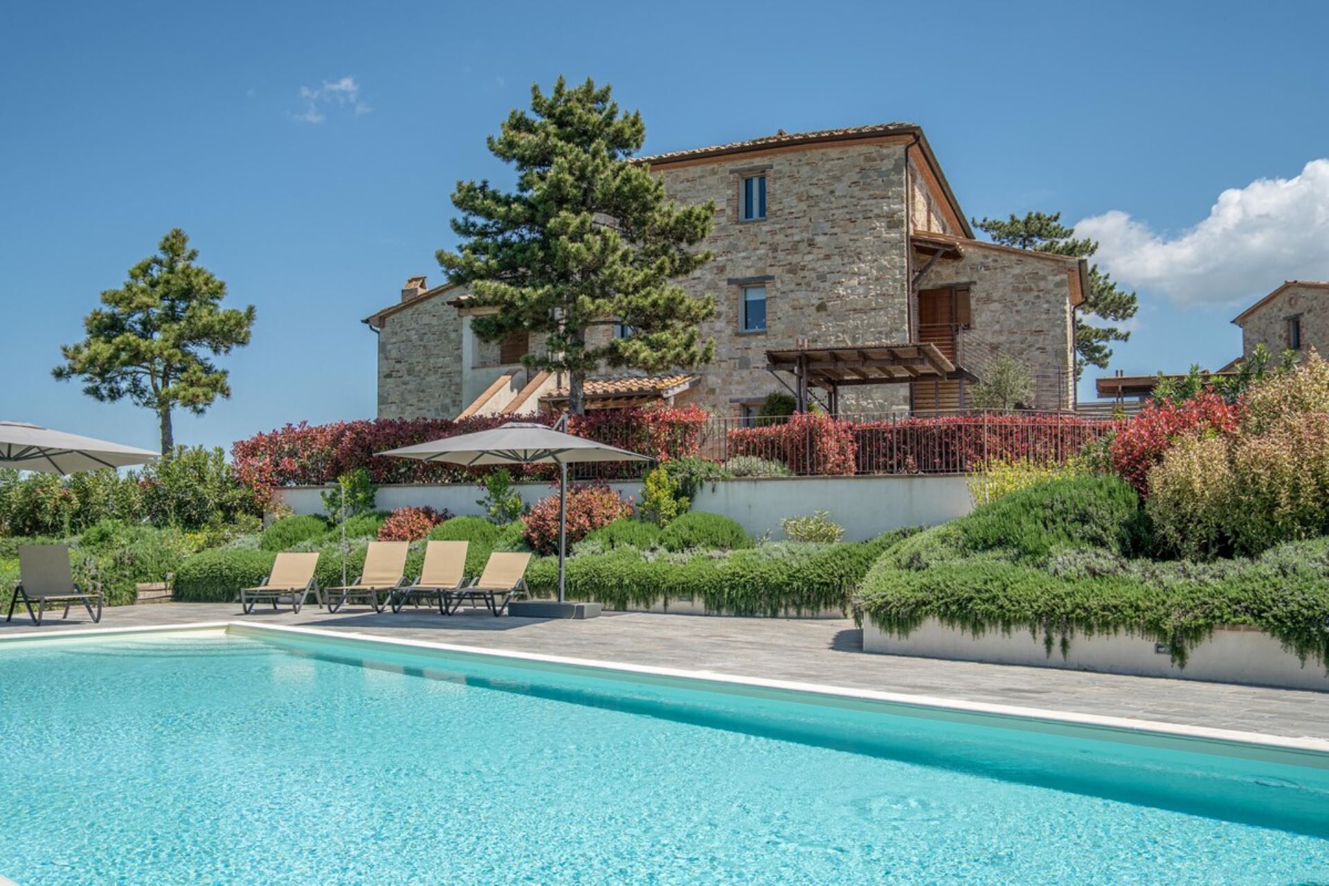 A stone building with a swimming pool and lounge chairs.