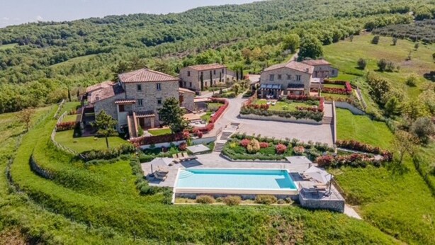Uma grande propriedade com piscina, vários edifícios e jardins bem cuidados.