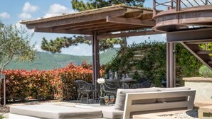 Um pátio externo com pérgola, assentos e vista para uma paisagem montanhosa.