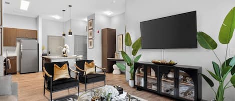 A modern living room with a flat-screen TV, a coffee table, and a dining area in the background.