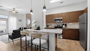 A modern kitchen with a central island, bar stools, wooden cabinets, stainless steel appliances, and a ceiling fan.