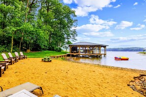 Ein Strand mit Liegestühlen, einer Holzkonstruktion und einer Mole, die in einen See führt.