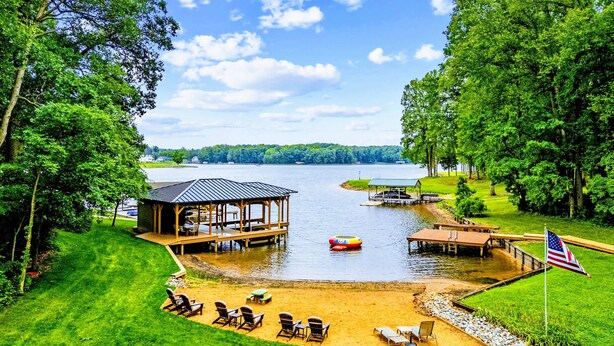 A lakeside property with a dock, a covered pavilion, and a sandy area with chairs. - Lake Anna Lakefront | Beach, Game Room, Hot Tub (Mineral)