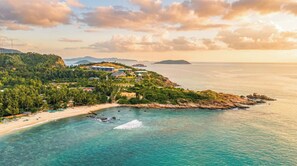 A coastal resort with a beach, clear turquoise waters, and a mountainous backdrop.