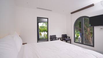 A bedroom with a large bed, a desk, two chairs, and a TV mounted on the wall.