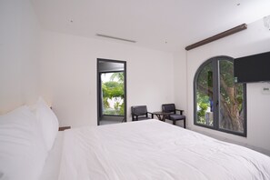 A bedroom with a large bed, a desk, two chairs, and a TV mounted on the wall.
