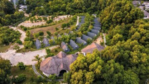 Ein Resort mit mehreren bungalowartigen Gebäuden, die in einer halbkreisförmigen Anordnung in üppigem Grün am Fluss gelegen sind.