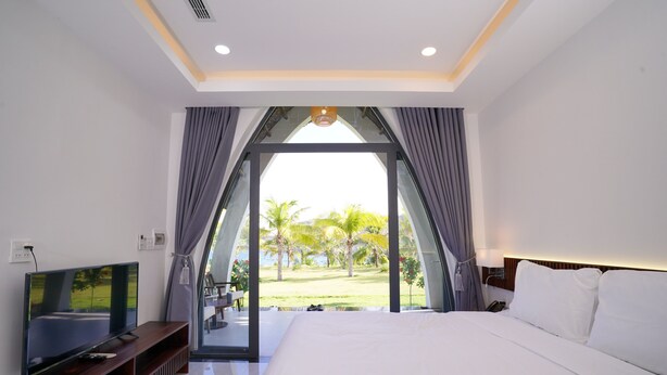 Ein Hotelzimmer mit Bett, Fernseher und Blick auf Palmen und einen Rasen.