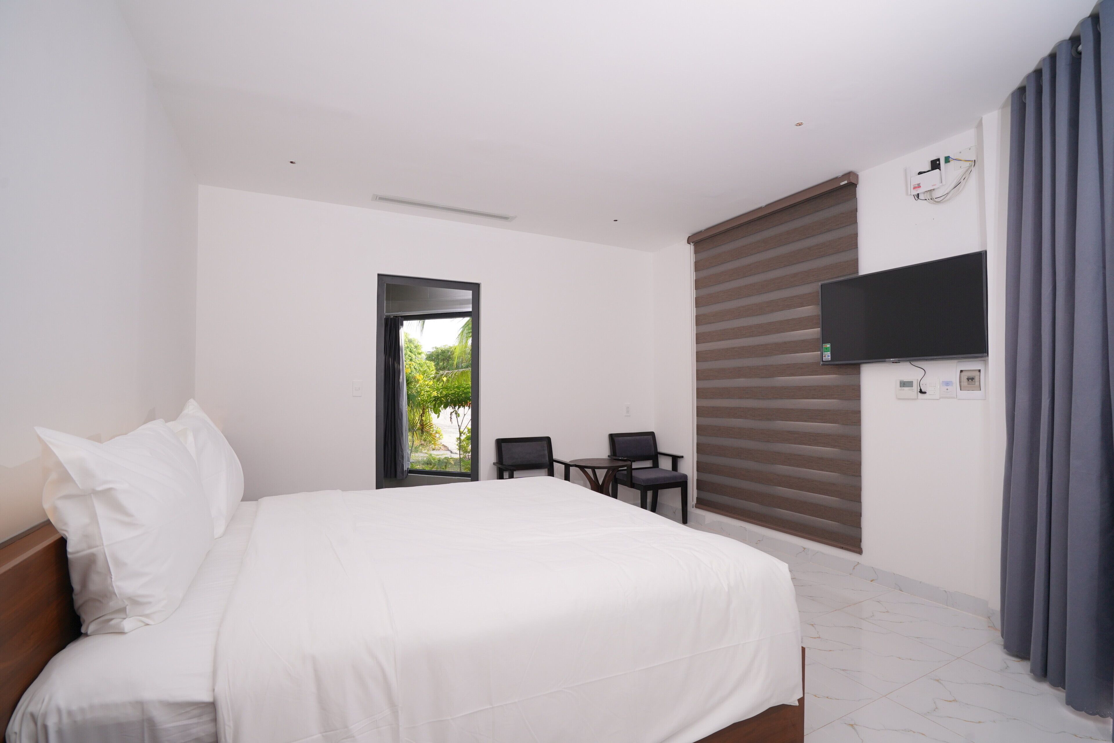 A bedroom with a bed, a TV, a window, and a door.