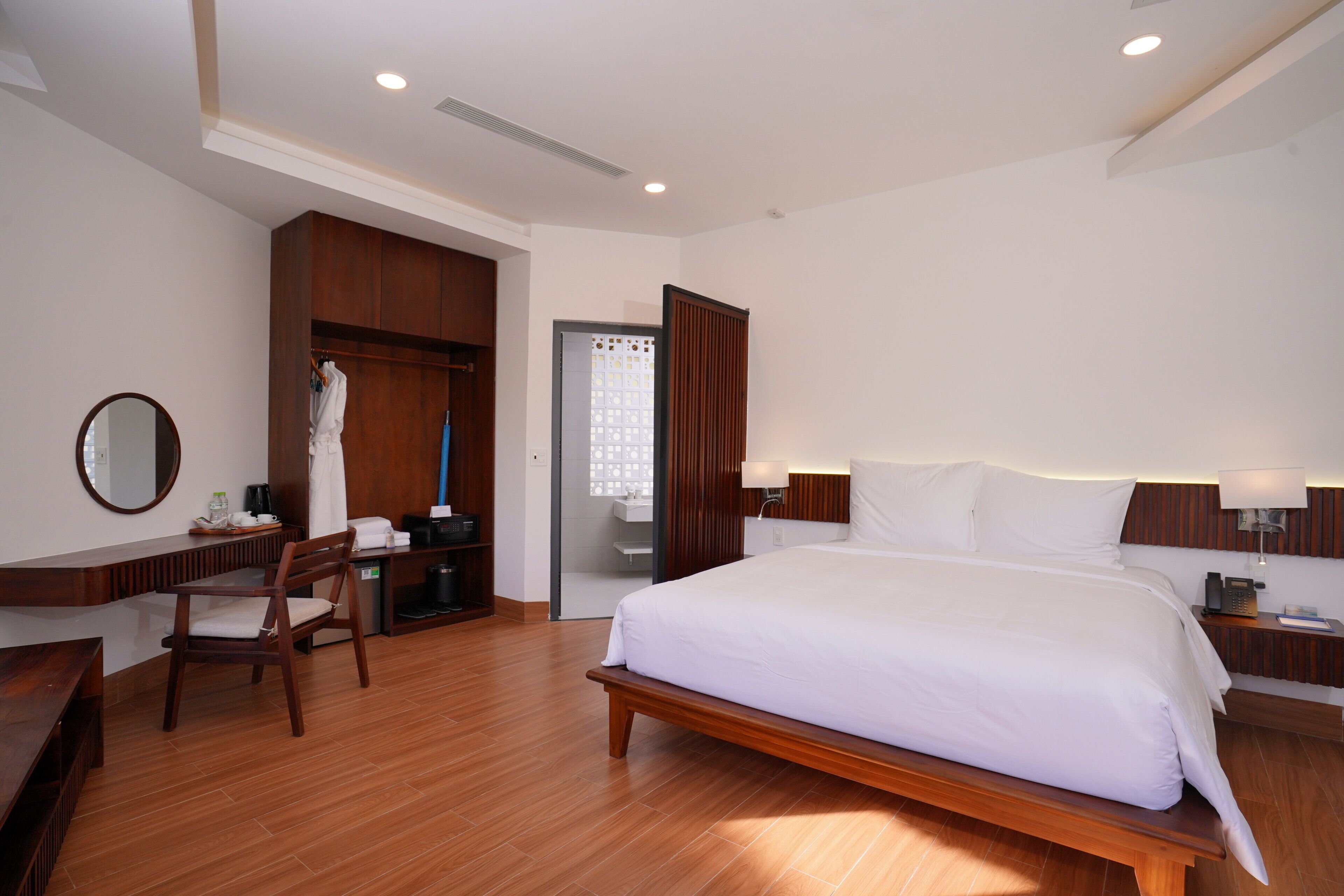 A hotel room with a large bed, wooden furniture, a desk, and a wardrobe.