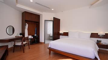 A hotel room with a large bed, wooden furniture, a desk, and a wardrobe.