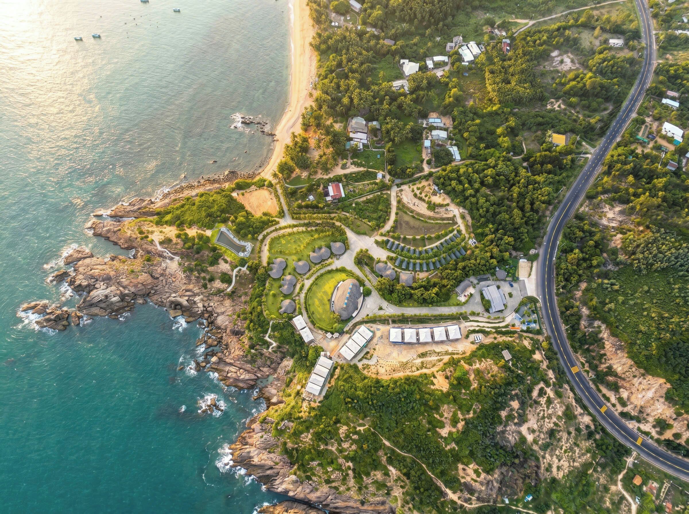 Vista aérea de una propiedad costera con un camino serpenteante, varios edificios y una playa.