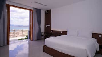 Habitación de hotel con una cama grande, cabecero de madera, un escritorio y vista al mar a través de un ventanal.