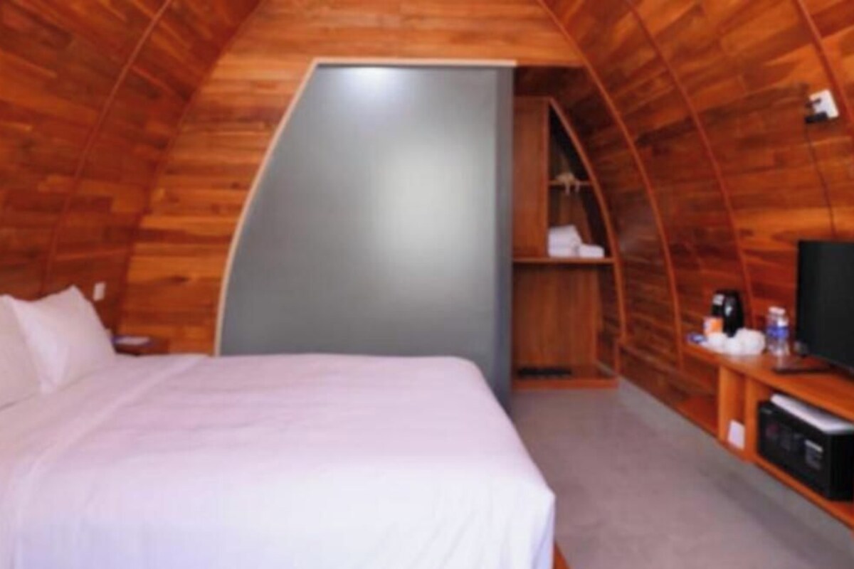 A single bed with white bedding in a room with wooden walls and a curved ceiling.