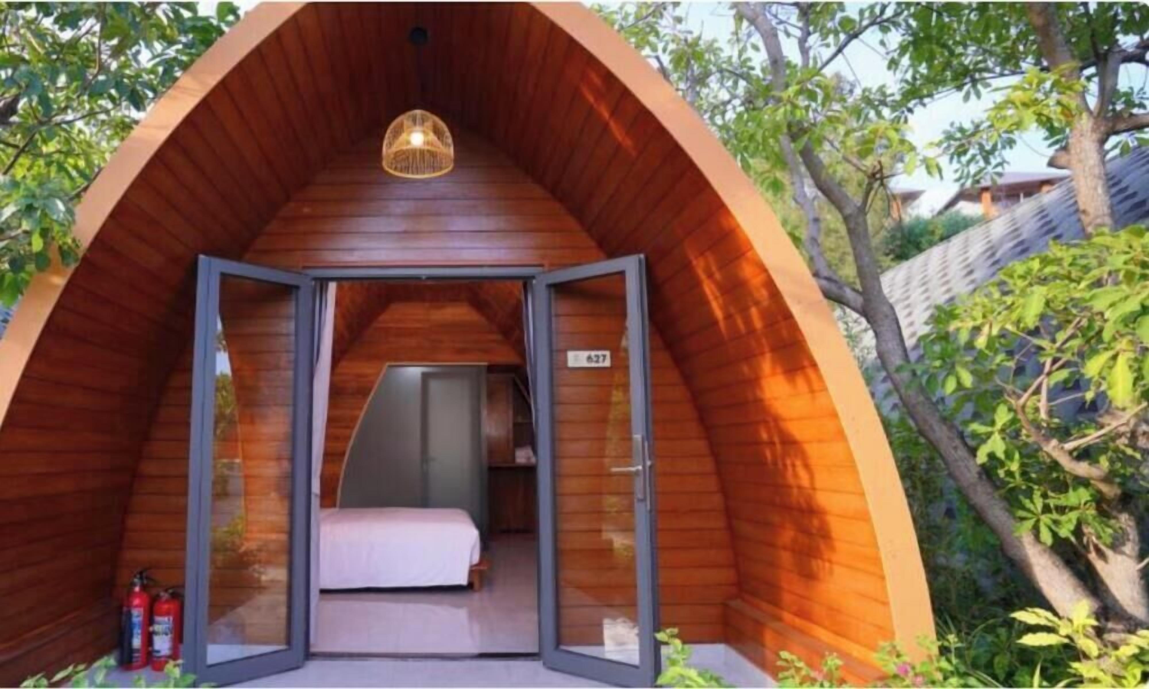 Uma estrutura em madeira com formato de cúpula, com uma cama e uma porta que dá para um quarto.