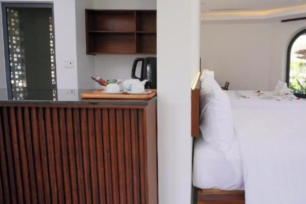A hotel room with a bed, a wooden panel wall, a small kitchenette, and a window with a view.