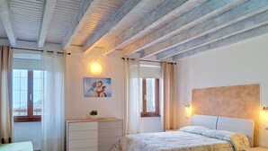 Une chambre à coucher comprenant un lit, des tables de chevet, une commode, une fenêtre avec des rideaux et un tableau accroché au mur.