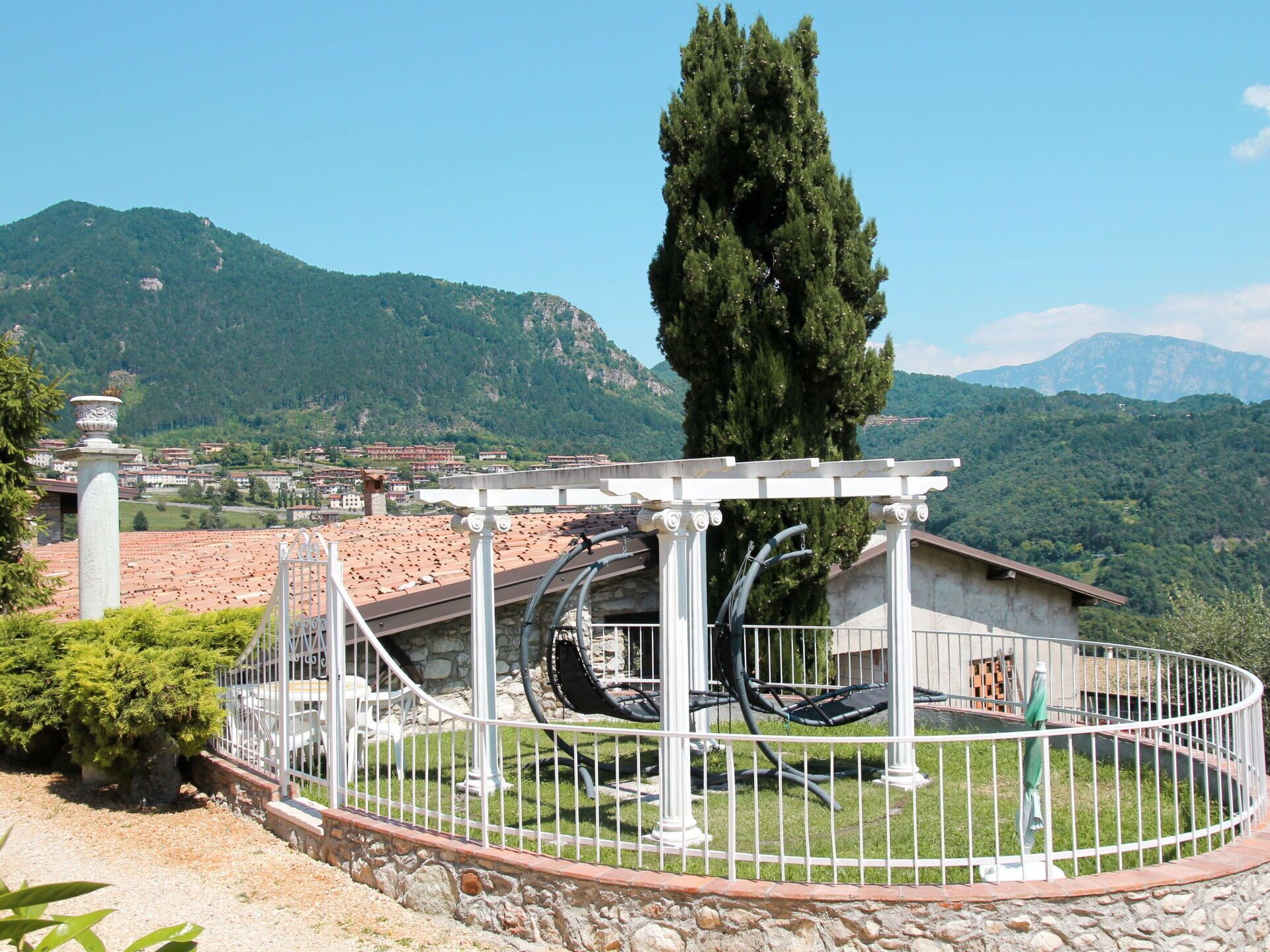 A gazebo with a stone base and white columns, surrounded by a white metal fence.