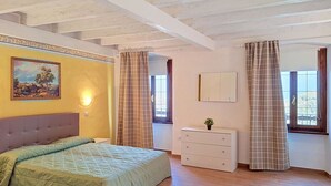 Un dormitori amb un llit, una petarrera, un quadre, un mirall i una finestra amb cortines.