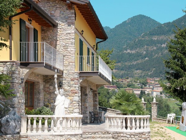 Ein Gebäude aus Stein mit Balkonen, einer Statue und einem Bergpanorama im Hintergrund.