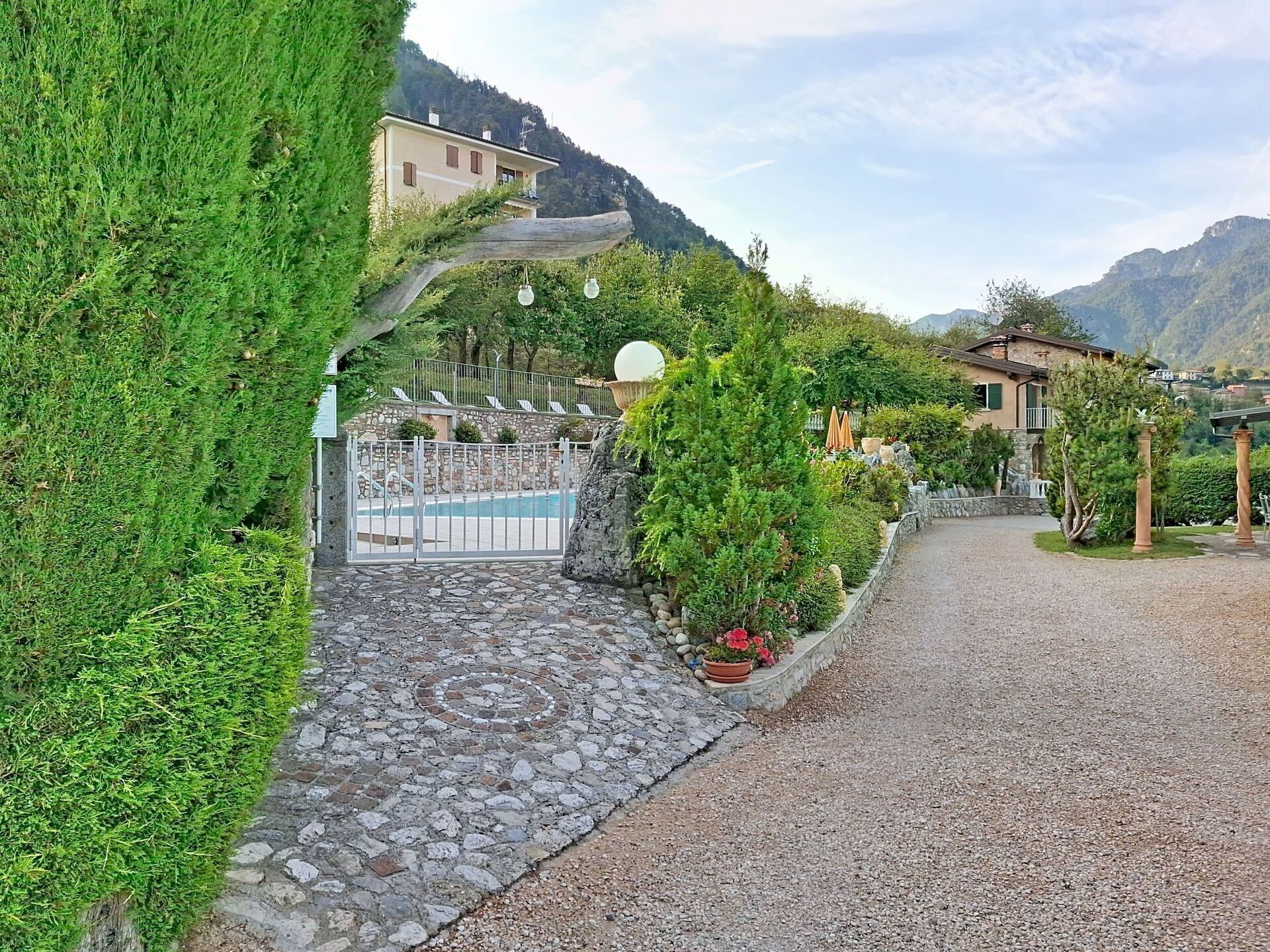 Un sentier mène à un espace piscine dont l’entrée est pavée de pierres, le tout étant entouré de verdure et surplombé par une chaîne de montagnes.