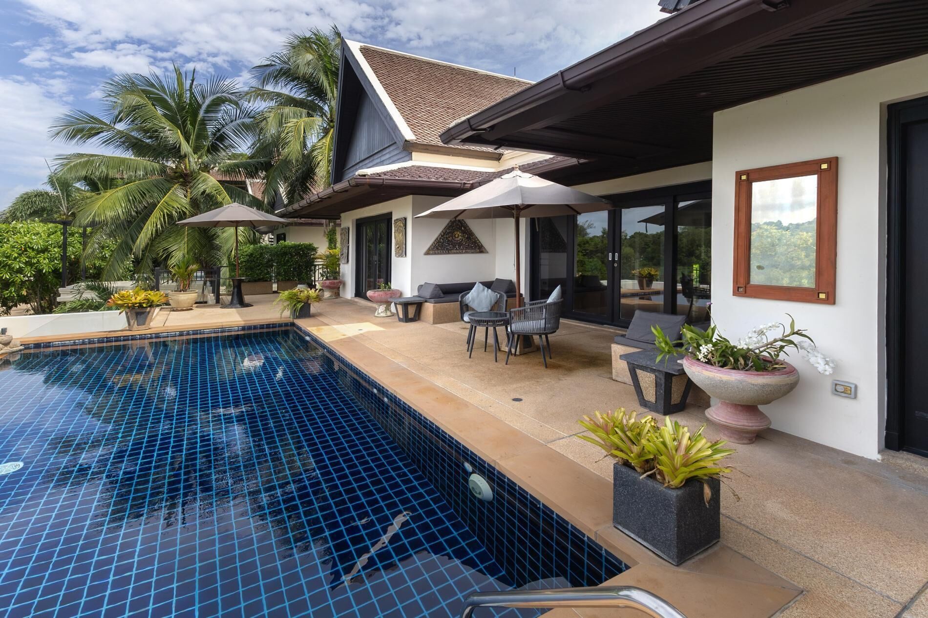 A modern outdoor pool area with a tiled floor, surrounded by potted plants and outdoor furniture.