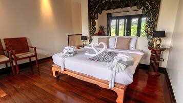 A hotel room with a large bed, two chairs, a decorative mirror, and a view of greenery outside.