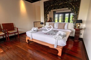 A hotel room with a large bed, two chairs, a decorative mirror, and a view of greenery outside. - Maan Tawan Front Beach Villa 12 (Choeng Thale)