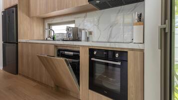 A modern kitchen with wood cabinetry, a built-in oven, a dishwasher, and a stainless steel refrigerator.