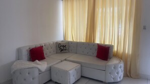 A white sectional sofa with red cushions, a white fluffy ottoman, and a cushion with 'Carpe Diem' text.