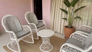 A room with two white wicker chairs, a small round table, a potted plant, and a window with curtains.