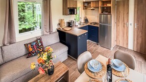 En kompakt opholdsstue med et tekøkken, en sofa med pude med blomstermønster og et spiseområde med et bord dækket til to.