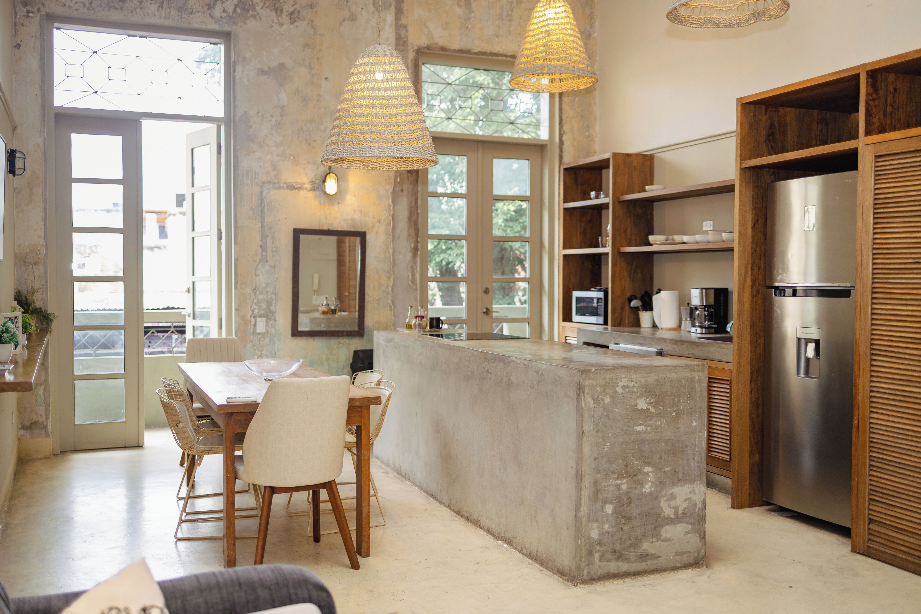 A kitchen with a concrete island, wooden shelves, and a stainless steel refrigerator.