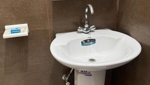 Un baño con un lavamanos pedestal blanco, un dispensador de toallas de papel y un dispensador de jabón.