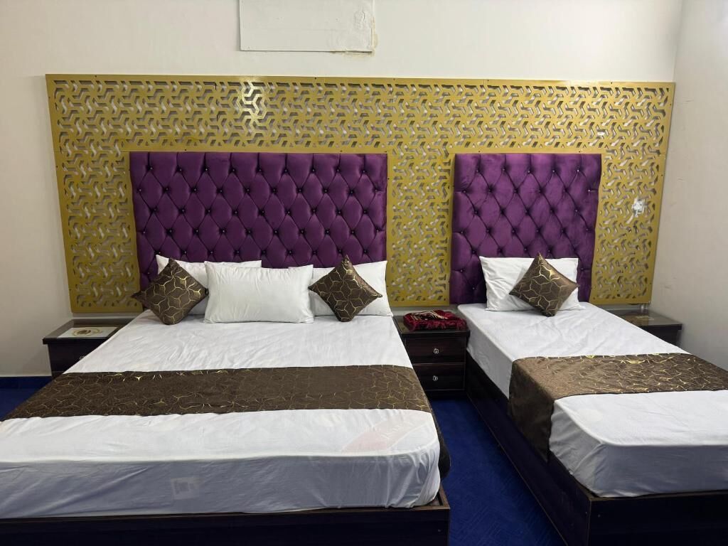 Habitación de hotel con dos camas, cada una con un cabecero morado acolchado, ropa de cama blanca y cojines decorativos.