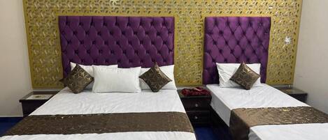 Habitación de hotel con dos camas, cada una con un cabecero morado acolchado, ropa de cama blanca y cojines decorativos.