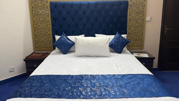 Una cama con cabecera capitonada, ropa de cama blanca y azul, y almohadas decorativas.