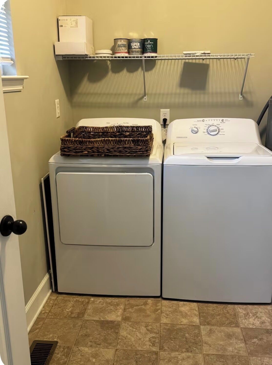 Une buanderie équipée de deux machines à laver et deux sèche-linge superposés, d’une étagère contenant des produits de nettoyage et d’un panier posé sur le sèche-linge.