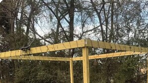 Un espacio de estar al aire libre con sillas tipo Adirondack y una chimenea, todo bajo una pérgola de madera.