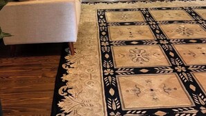 Una sala de estar con sofá, alfombra estampada, comedor con sillas y cocina al fondo.