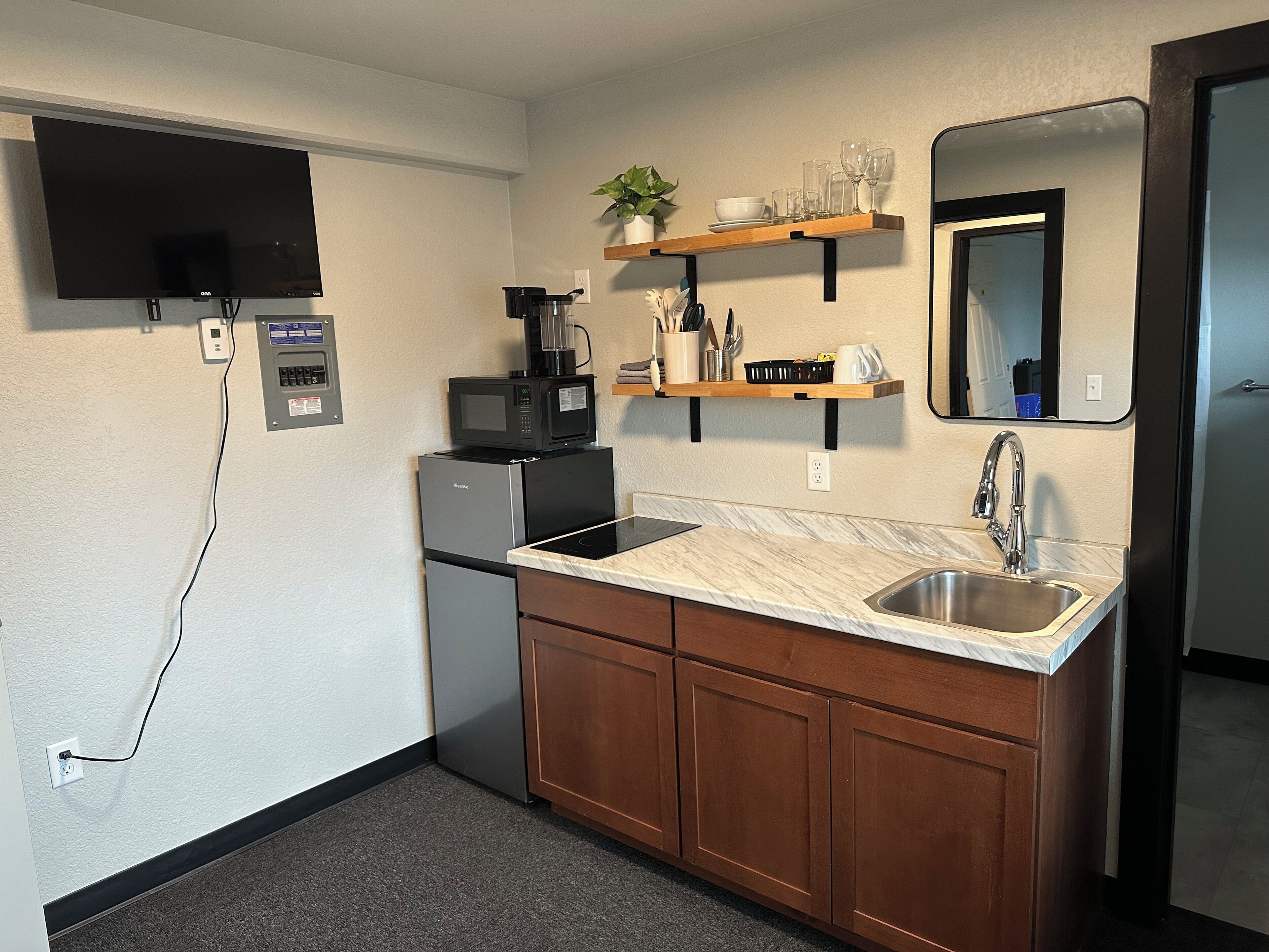 A compact kitchen with a built-in microwave, a coffee maker, a sink, and a small refrigerator.