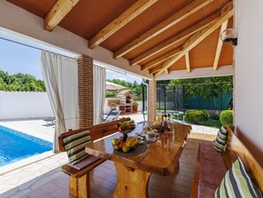 An outdoor dining area with a pool view, wooden beams, and a brick pillar. - Nevenka by Interhome (Barban)