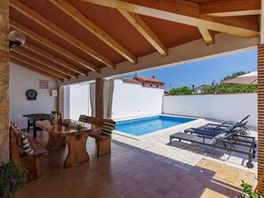 Un espacio al aire libre techado con piscina, mobiliario y una mesa de fútbol.
