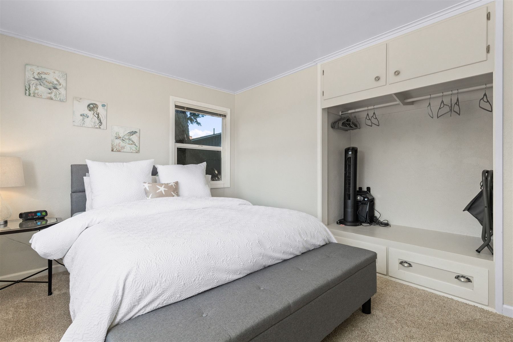 A bedroom with a bed, a nightstand, a window, and a wardrobe with hanging items.