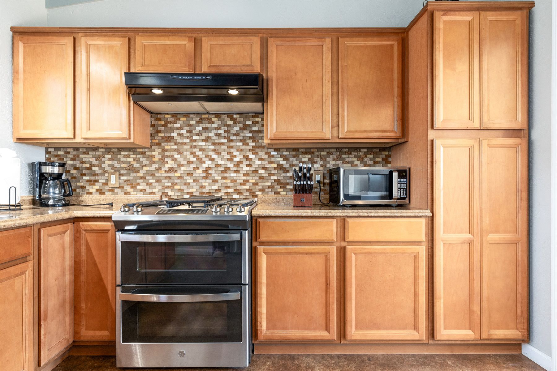 Una cocina con armarios de madera, estufa de acero inoxidable, microondas y cafetera.