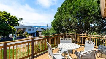 A wooden deck with outdoor furniture, a view of a house, and a large tree.