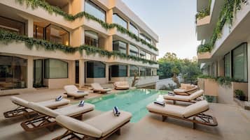 Un edificio moderno con piscina, sillones de descanso y áreas verdes en los balcones.